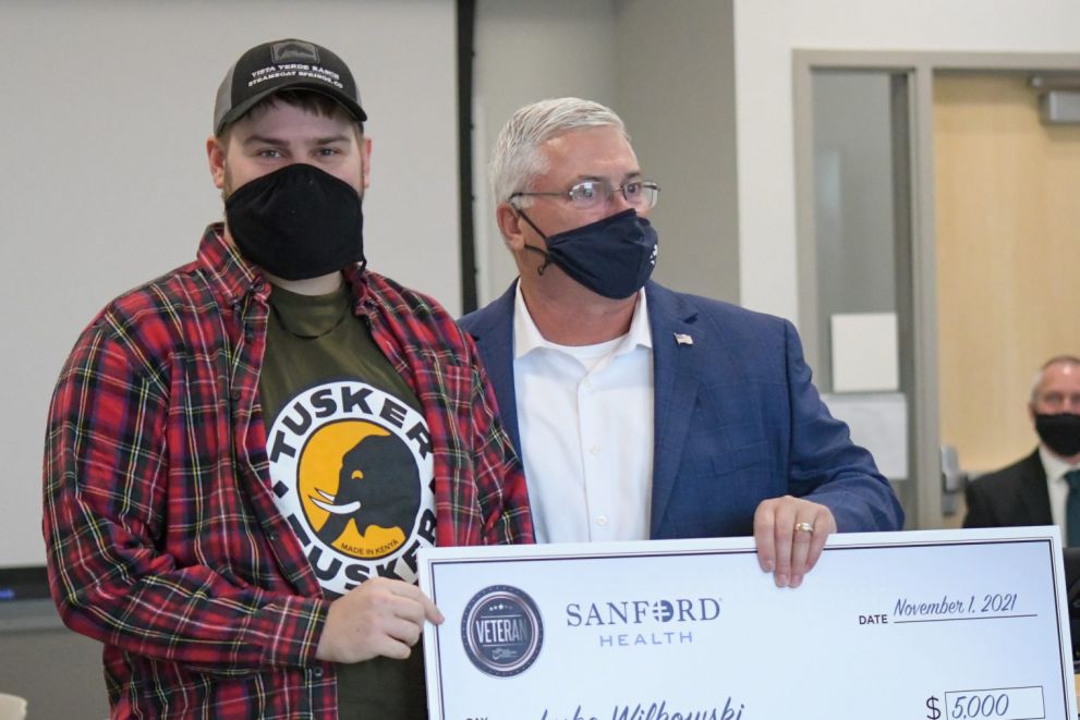 Captain Paul Weckman, director of veteran and military affairs at Sanford Health, presents an oversized check of $5000 to junior nursing student Luke Wilkowski, a veteran Specialist in the U.S. Army.