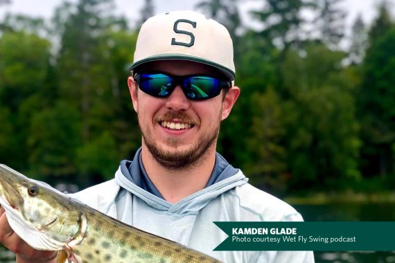 A photo of a man with sunglasses wearing a white baseball cap with a green letter S on the front, holding a large fish.