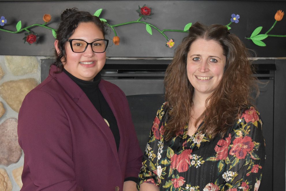 Ann Humphrey and Hillary Barron stand in front of the fireplace in the American Indian Resource Center's Gathering Room at Bemidji State University.